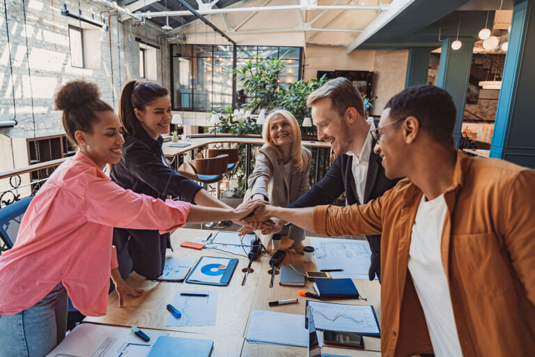 a group of people standing around a work table put hands in a pile