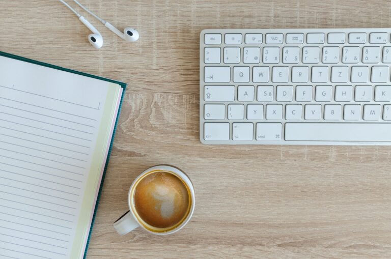 a cup of coffee sitting between a keyboard and pad of paper