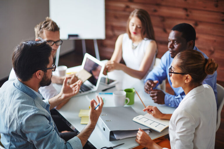 a group of people talking around a table and laptop