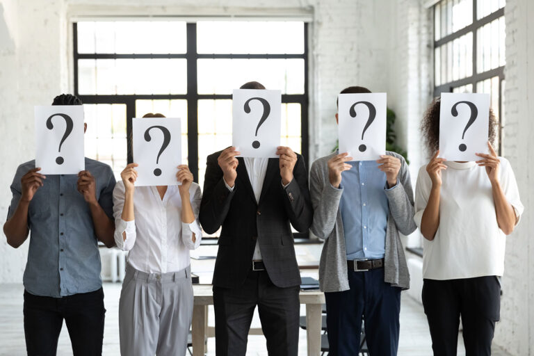 five people standing in an office holding a paper with a question mark in front of their faces