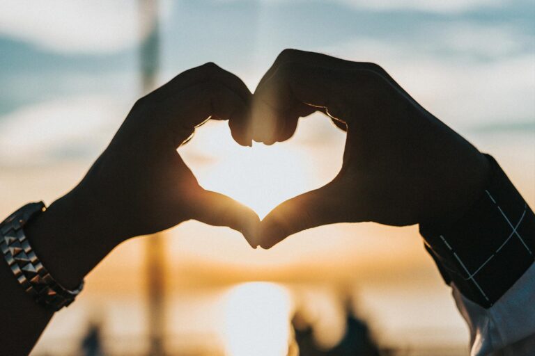 Person makes heart hands in front of sunset