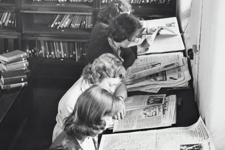 Old photo of 4 people reading newspapers.