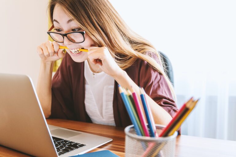 a young woman chewing on pencil looking at laptop screen