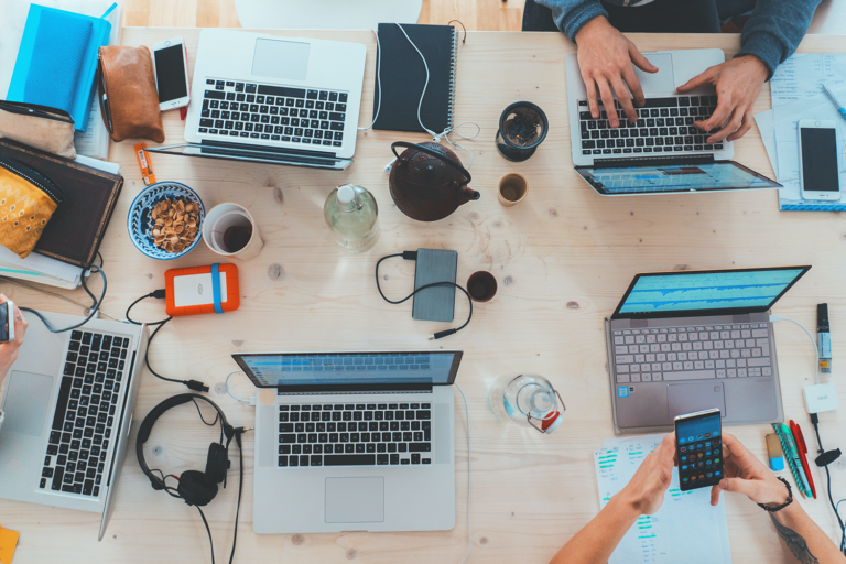 A number of laptops and devices at a shared work table.