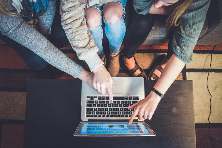 arms of three people pointing to a laptop screen