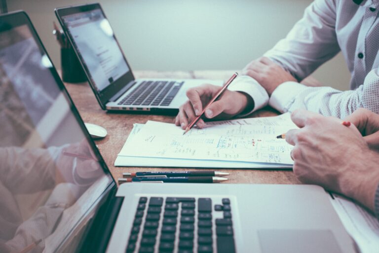 two people looking over financial records on two laptop screens