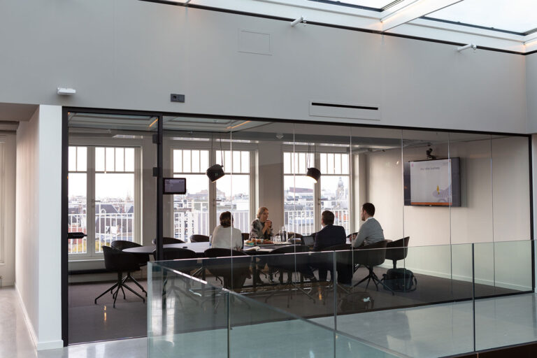 four people sitting in a glass-enclosed conference room