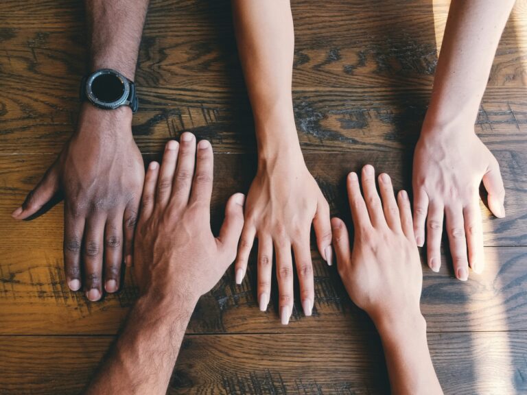 a close up of 5 hands lined up on a wood desktop