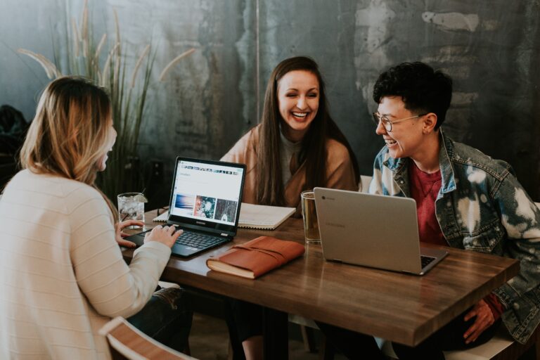 3 smiling people sitting at a table with laptops