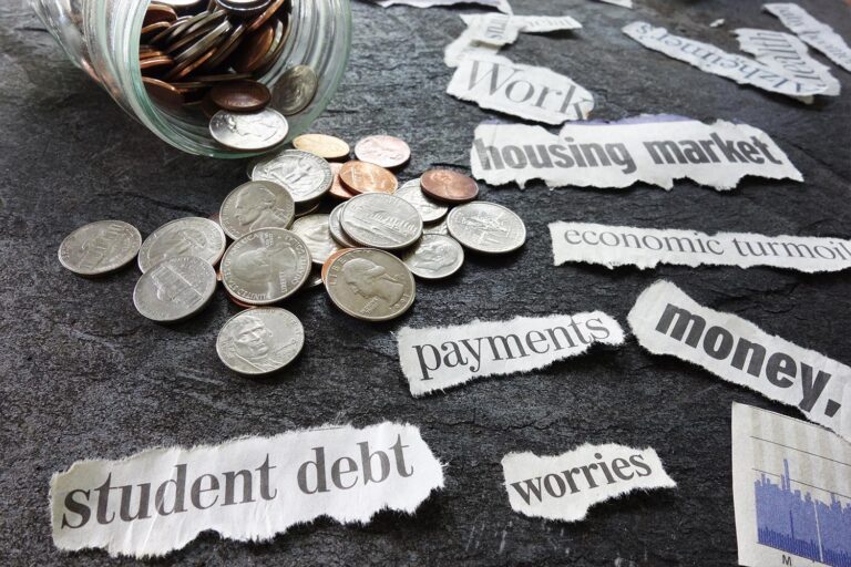 A jar of coins spilled, torn pieces of newspaper with words like student debt, worries, payments, etc.