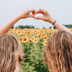 Two girls make a heart shape with their hands in a sunflower field