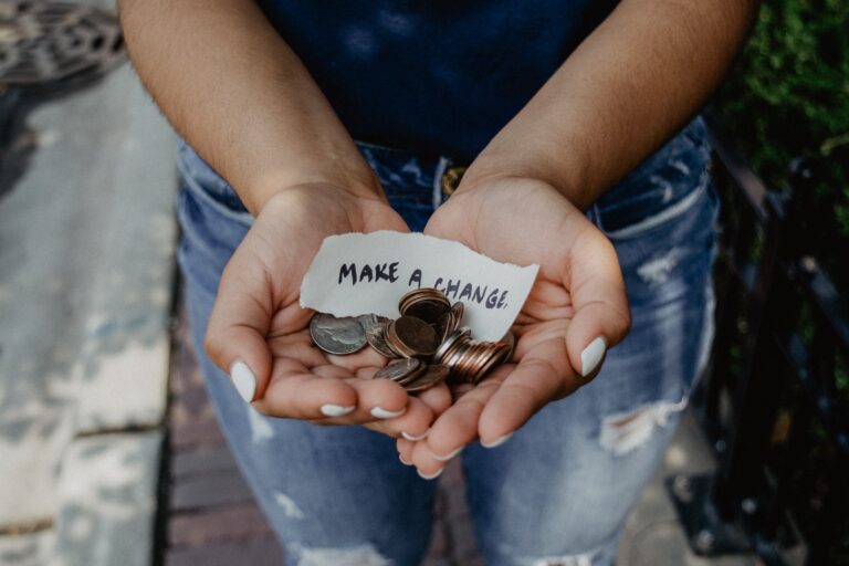 a person holding their hands out with coins and a small paper with "make a change" written on it