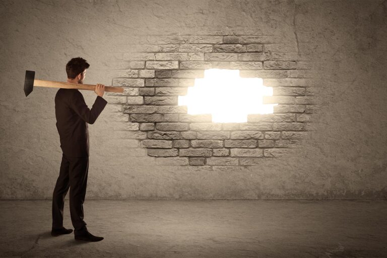 Man with sledgehammer looks at light coming through broken wall