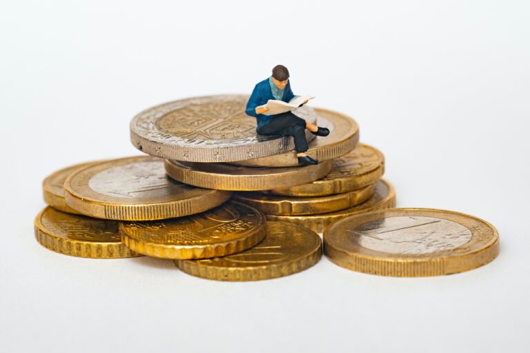 small figurine of a man reading a book sitting on some coins