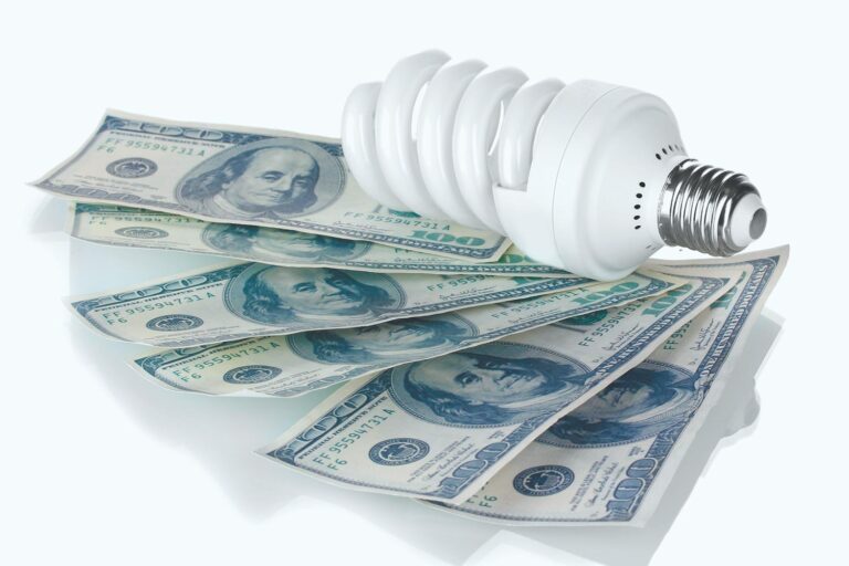 An energy saving light bulb on top of 5 hundred dollar bills