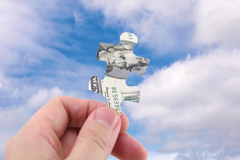 Hand holds up a $20 bill in the shape of a puzzle piece