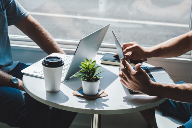 two people sitting at a table with 2 laptops