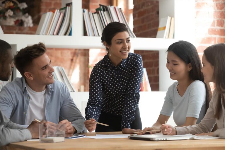 Woman stands at table with other people around it