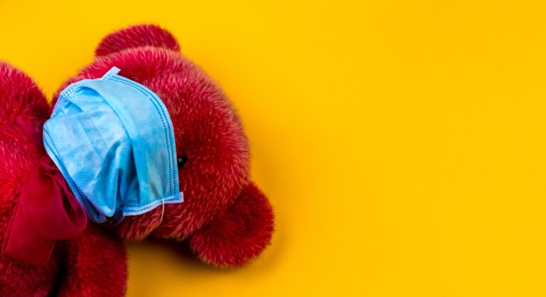 a red stuffed animal bear wearing a medical face mask on a yellow background