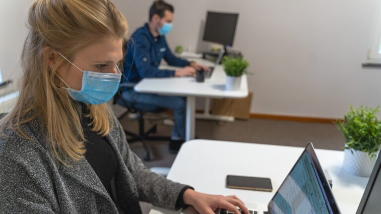 a woman wearing a medical face mask working on a laptop