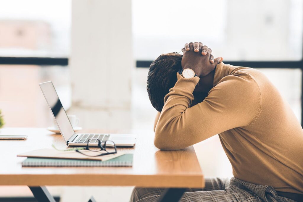 a person sitting at a table with a laptop with hands clasped above their head.