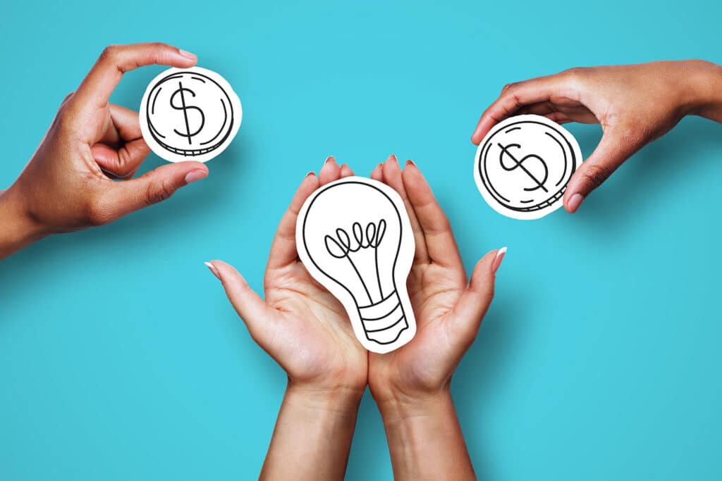 hands holding paper cutouts of coins and a lightbulb to illustrate nonprofit fundraising 