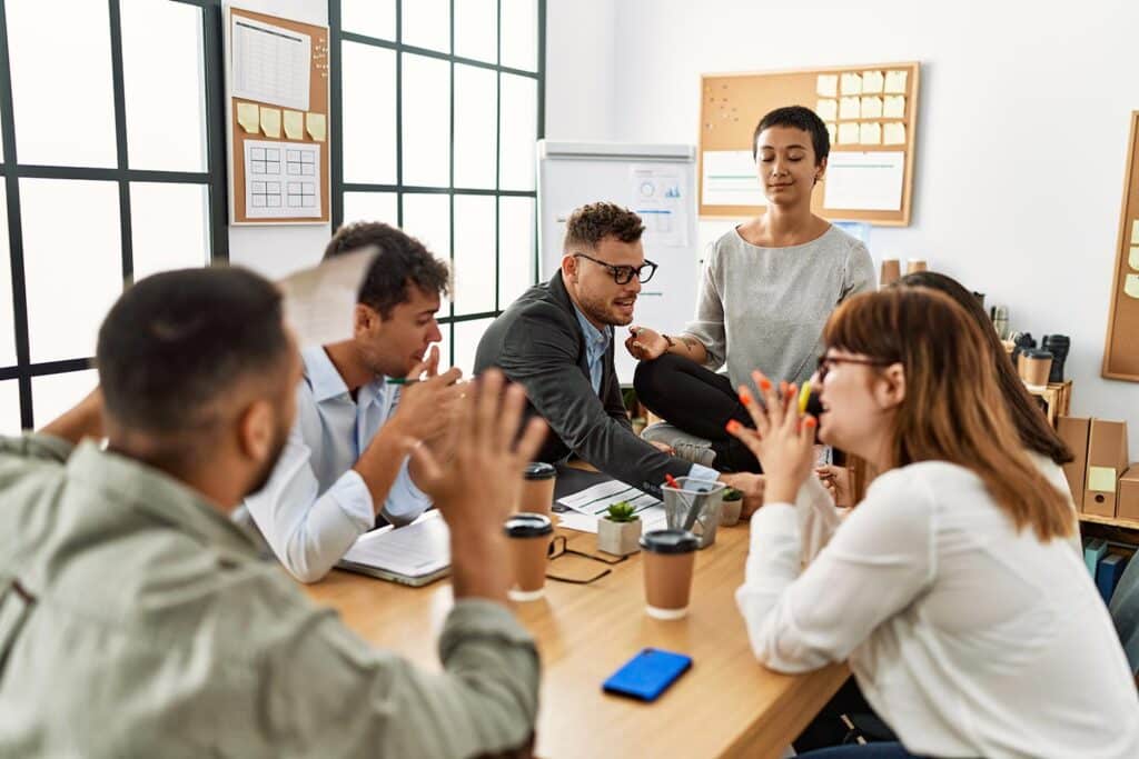 a calm woman sits on the table where a business arguement is happening among several people