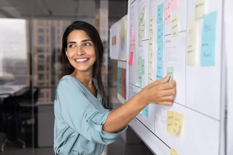 a woman pointing at a white board with post-it notes